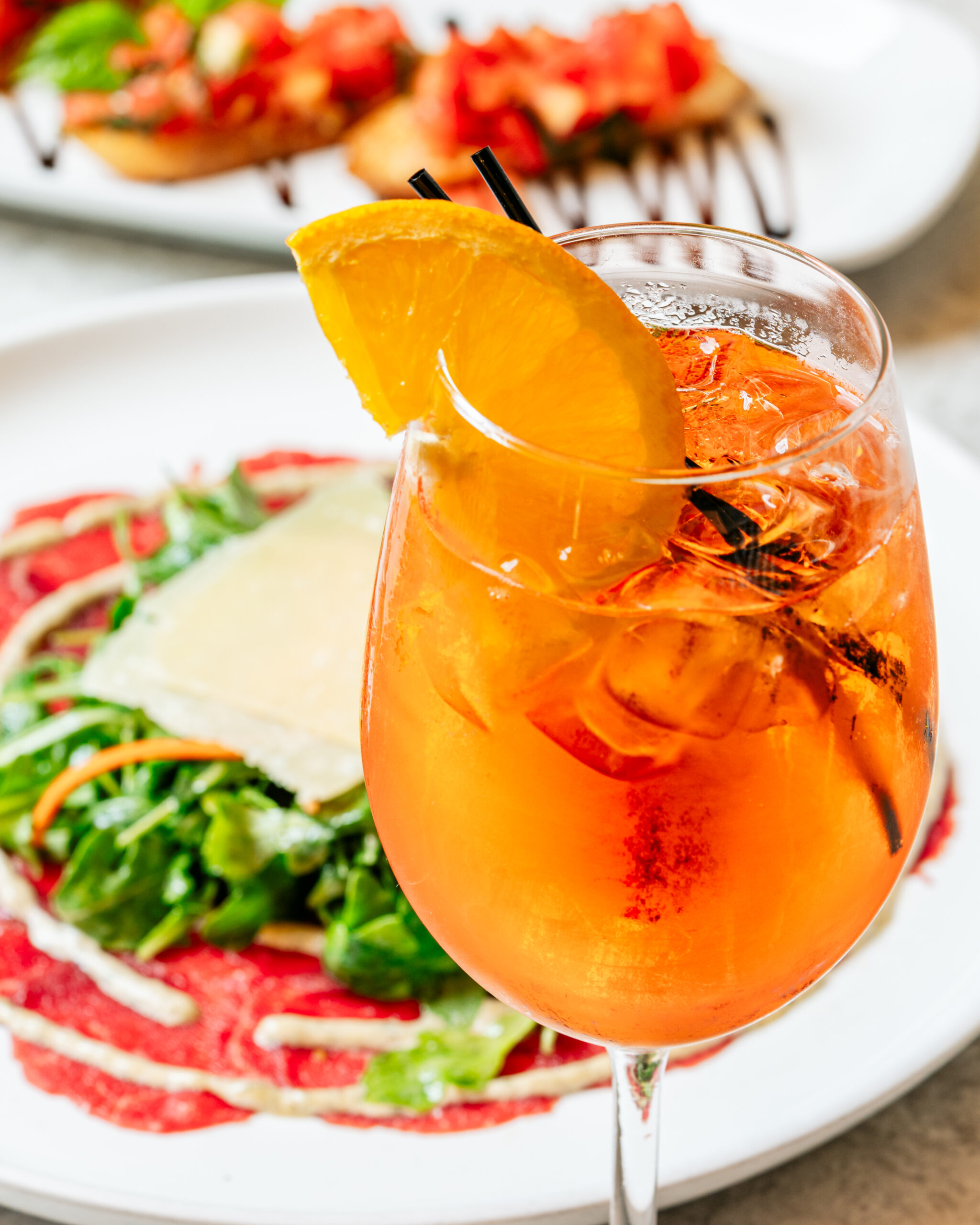 Orange cocktail with ice, garnished with orange slice, and salad in background