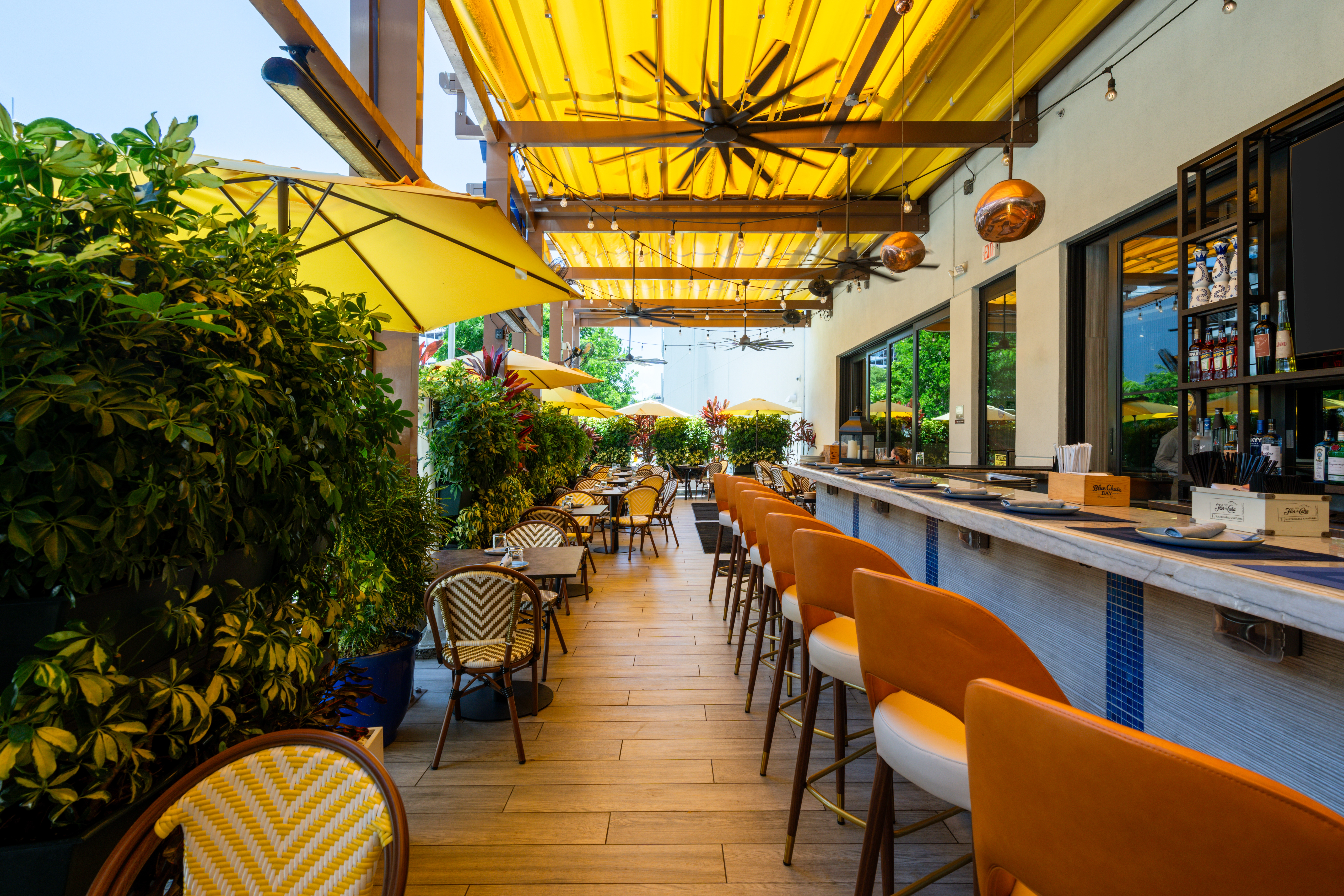 Outdoor restaurant patio with yellow umbrellas, orange chairs, wooden floors