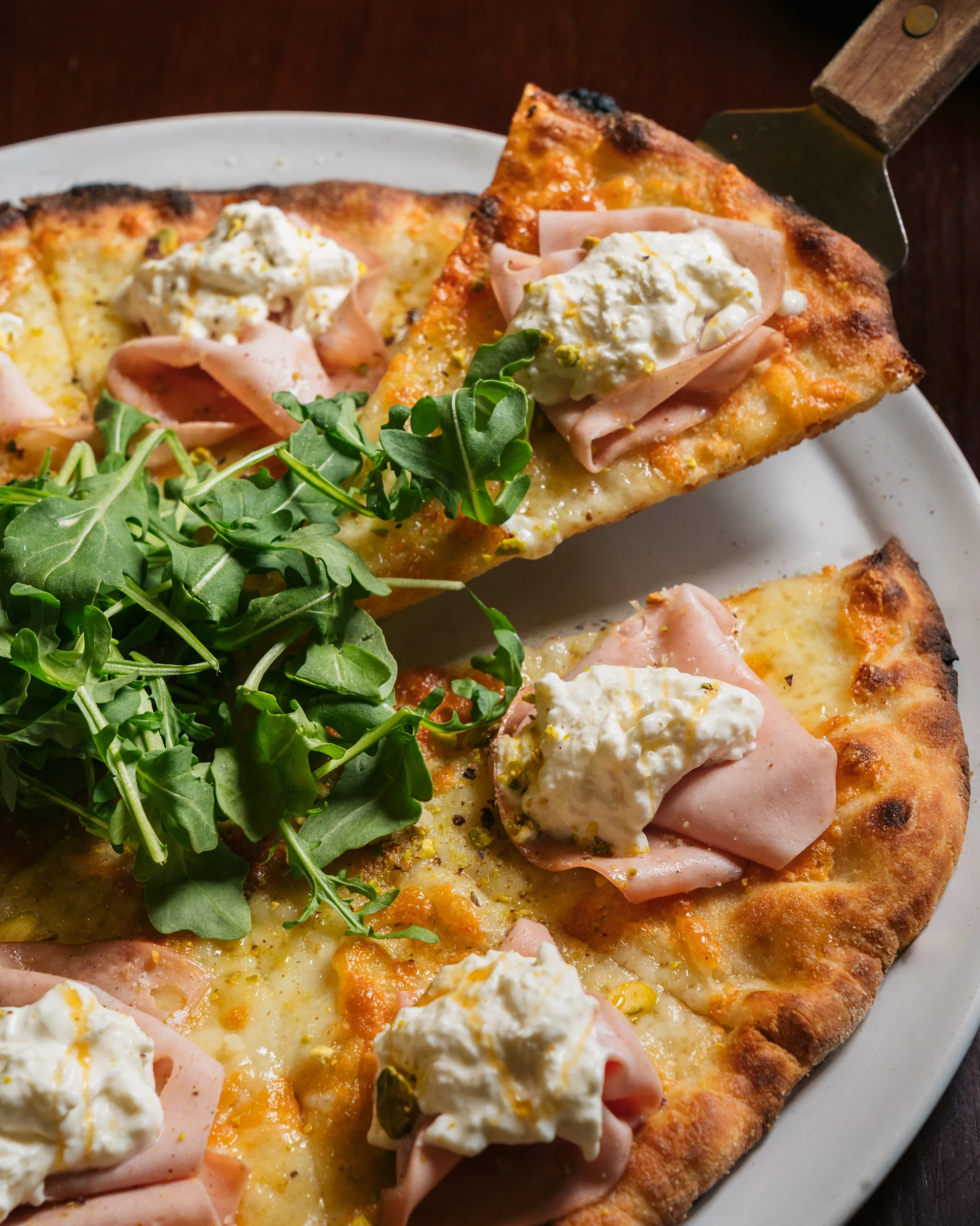 Gourmet pizza slice with mortadella, ricotta, and arugula